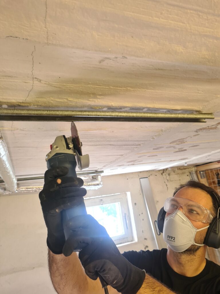 Heimwerker mit Schutzbrille trennt ein Metallprofil an der Decke mit einem Bosch Winkelschleifer.